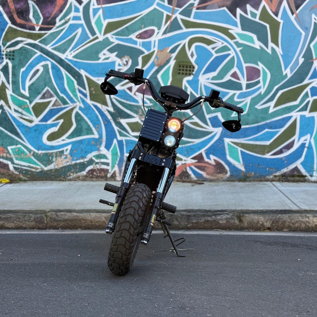 FONZ NKD Electric Motorcycle parked on a street with a colorful mural in the background